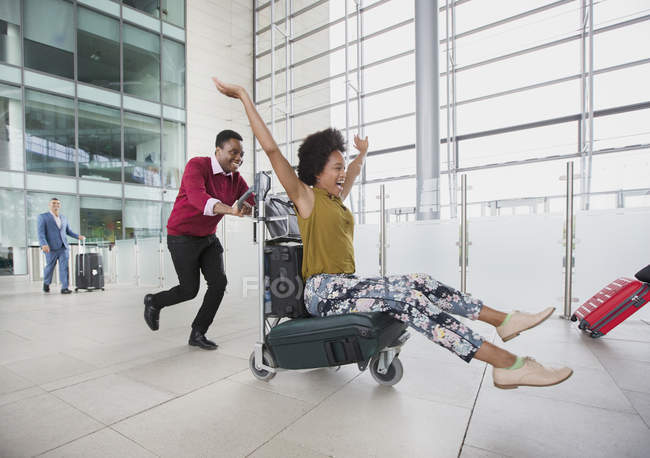Verspieltes Paar läuft mit Gepäckwagen in Flughafen — Stockfoto