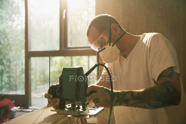 Construction worker with tattoo using electric saw to cut wood — Stock Photo