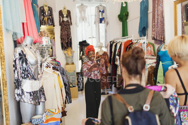 Young women friends with camera phone shopping in clothing store — Stock Photo