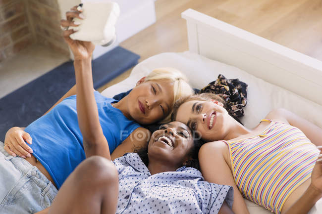 Young women friends using instant camera on bed — Stock Photo
