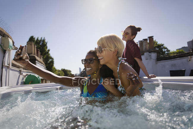 Young women friends taking selfie in sunny rooftop hot tub — Stock Photo