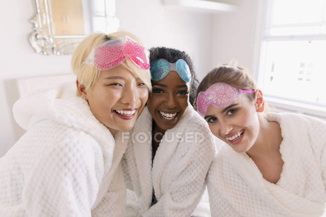 Portrait happy young women friends in bathrobes and eye masks — Stock Photo