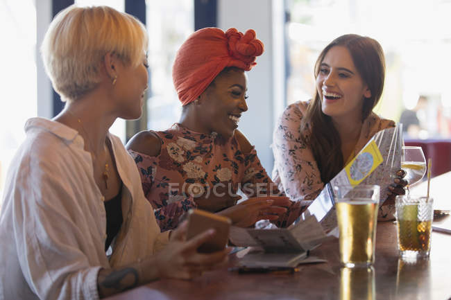 Щасливі молоді жінки друзі дивляться на мапу, п'ють коктейлі в барі — стокове фото