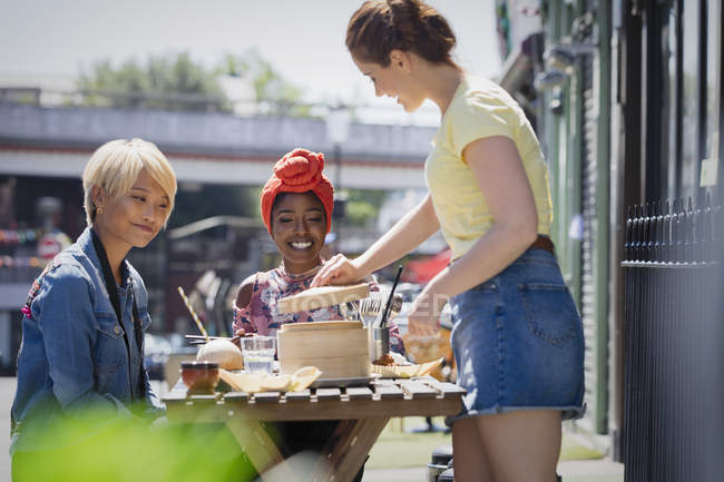 Молодые женщины-друзья наслаждаются обедом дим в солнечном кафе на тротуаре — стоковое фото