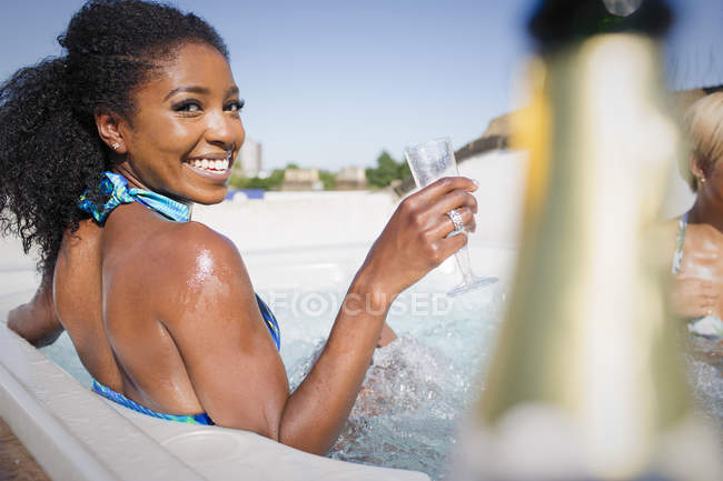 Retrato confiante, jovem despreocupada bebendo champanhe na banheira de hidromassagem ensolarada — Fotografia de Stock