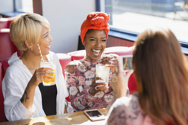 Jóvenes felices amigas tomando cócteles y riendo en el restaurante - foto de stock
