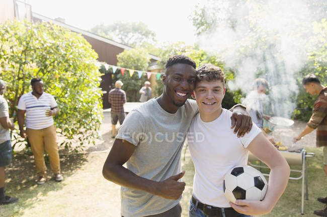 Ritratto fiducioso giovani uomini con pallone da calcio godendo barbecue cortile — Foto stock