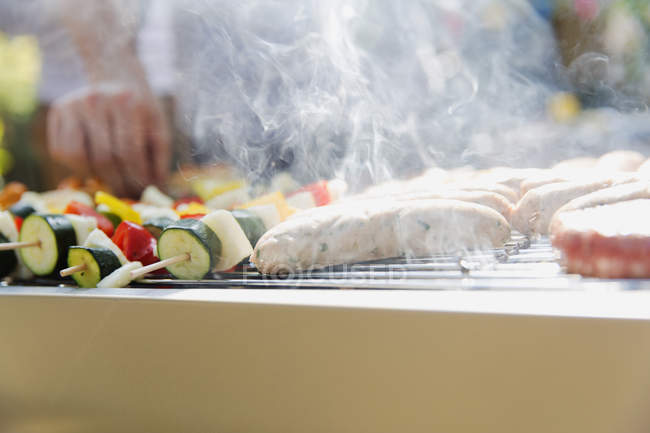 Close up sausages and vegetable skewers cooking, steaming on barbecue grill — Stock Photo