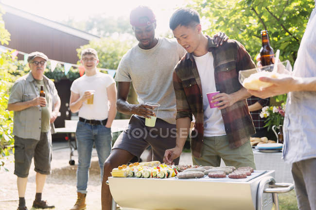 Amigos masculinos disfrutando de barbacoa en el soleado patio trasero de verano - foto de stock