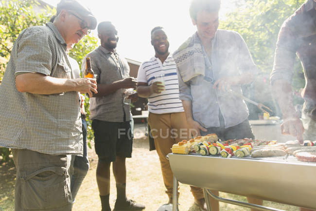 Male friends drinking beer around barbecue grill in backyard — Stock Photo