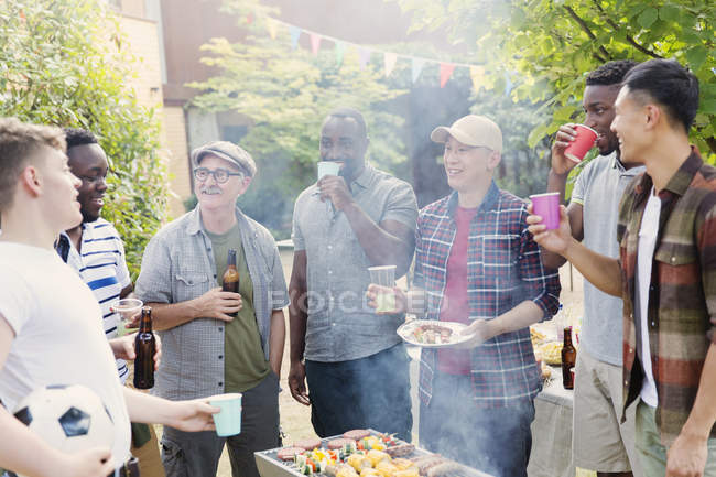 Male friends drinking beer around barbecue grill in backyard — Stock Photo
