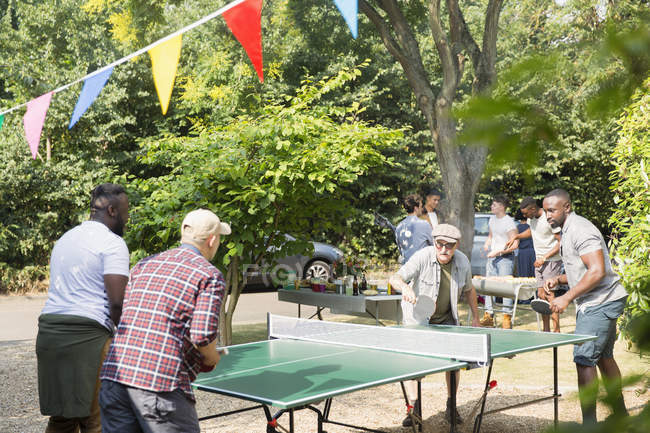 Amigos masculinos jugando ping pong en el patio trasero soleado - foto de stock
