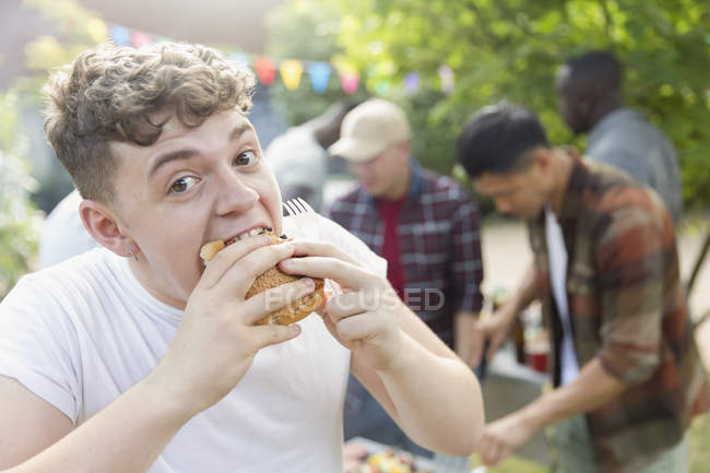 Retrato fome adolescente menino comer hambúrguer no quintal churrasco — Fotografia de Stock