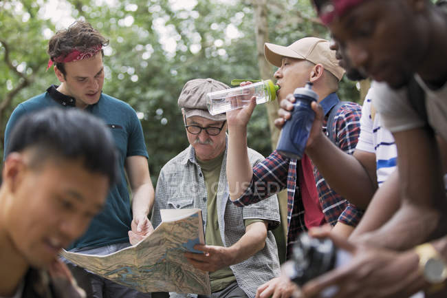 Група чоловіків з картою та пляшками води, що ходять у лісі — стокове фото