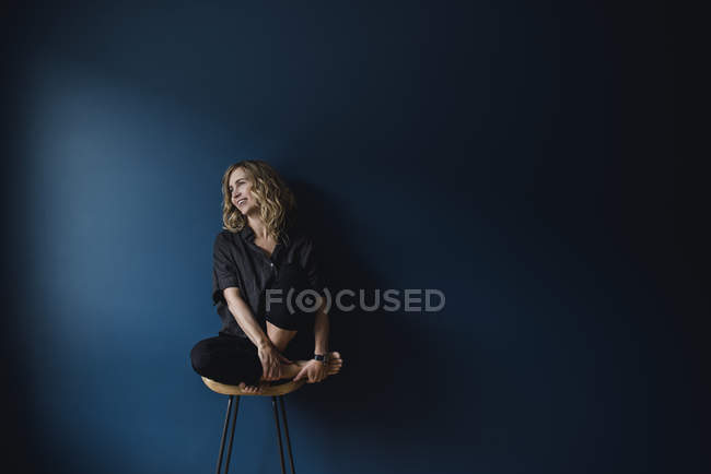 Retrato mujer despreocupada sentada en el taburete sobre fondo azul - foto de stock