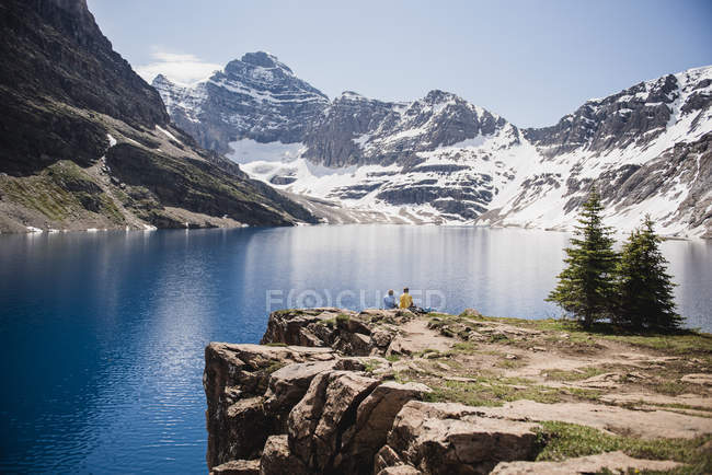 Casal sentado no penhasco com vista para a tranquilidade, montanhas ensolaradas e lago, Yoho Park, British Columbia, Canadá — Fotografia de Stock