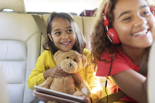 Happy sisters with teddy bear riding in back seat of car — Stock Photo