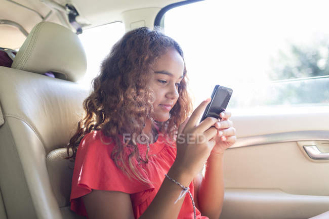 Mädchen benutzt Smartphone auf Rücksitz des Autos — Stockfoto