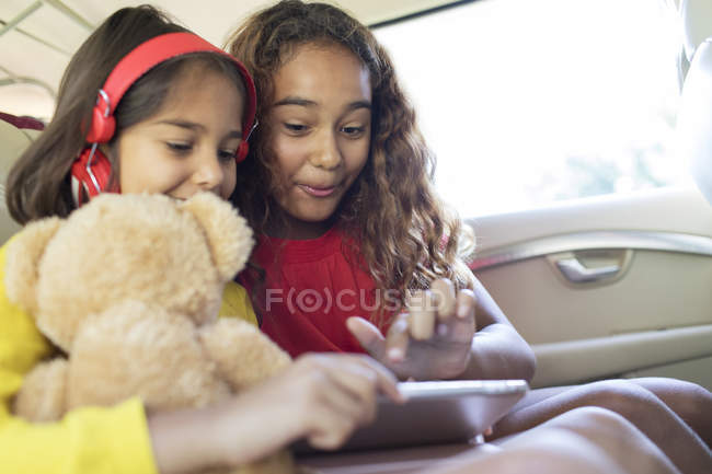 Сестры, использующие цифровой планшет на заднем сиденье автомобиля — стоковое фото