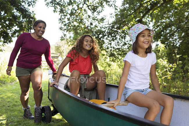 Happy mother and daughters pushing canoe in woods — Stock Photo