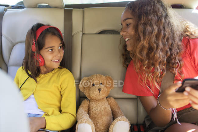 Sisters and teddy bear riding in back set of car — Stock Photo