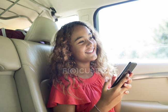 Усміхнена дівчина використовує смартфон на задньому сидінні автомобіля — стокове фото