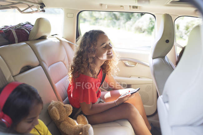 Entre fille avec téléphone intelligent équitation sur le siège arrière de la voiture en voyage sur la route — Photo de stock