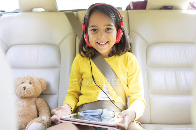 Портрет улыбается, уверенная девушка смотрит кино с наушниками и цифровым планшетом на заднем сиденье автомобиля — стоковое фото