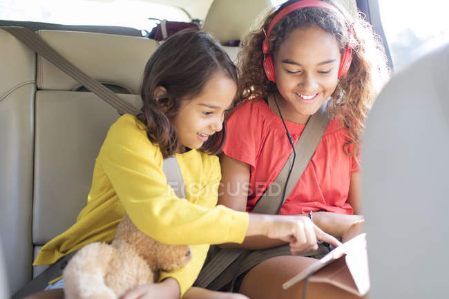Сестри використовують цифровий планшет на задньому сидінні автомобіля — стокове фото