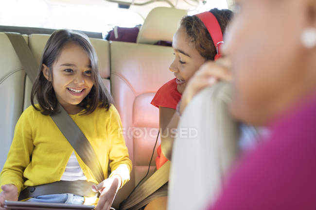 Irmãs felizes andando no banco de trás do carro com tablet digital — Fotografia de Stock