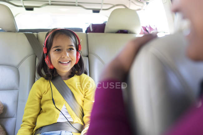 Chica sonriente con auriculares montando en el asiento trasero del coche - foto de stock