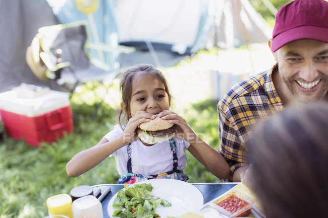 Padre e hija comiendo hamburguesas barbacoa en el camping - foto de stock