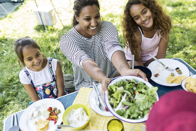 Happy mother and daughters enjoying salad lunch at campsite table — Stock Photo