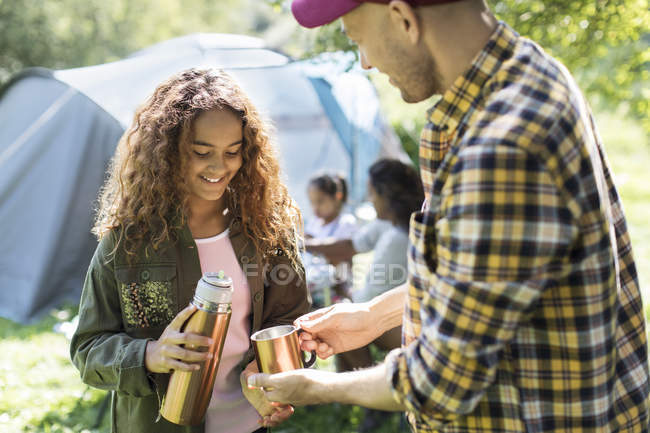 Daughter pouring coffee from insulated drink container for father at campsite — Stock Photo