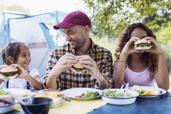 Happy father and daughters eating barbecue hamburgers at campsite — Stock Photo