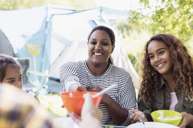 Madre e hijas sonrientes disfrutando del almuerzo en el camping - foto de stock