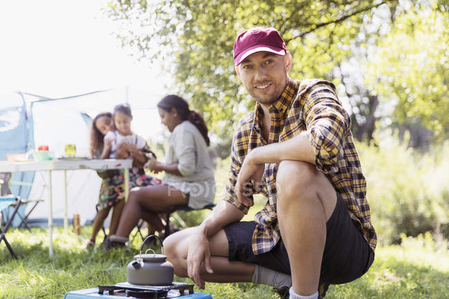 Portrait confident man heating teapot on camping stove at sunny campsite — Stock Photo