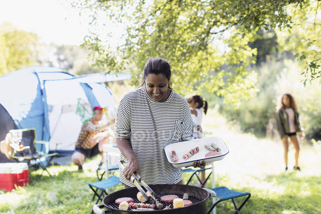 Smiling woman barbecuing lunch for family at campsite — Stock Photo