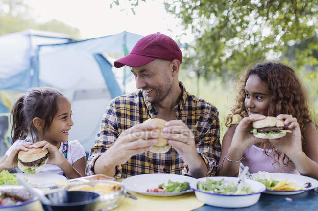 Pai e filhas desfrutando de churrasco hambúrguer almoço no acampamento — Fotografia de Stock
