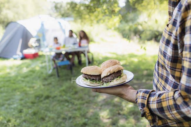 Pai servindo hambúrgueres de churrasco para a família no acampamento — Fotografia de Stock
