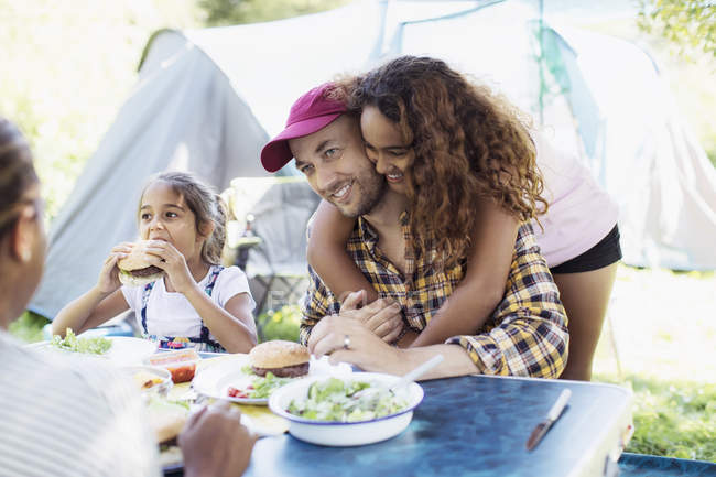 Affectionate daughter hugging father eating lunch at campsite — Stock Photo