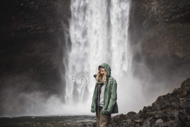 Lächelnde Wanderin in Regenjacke am Wasserfall, Pfeifer, britische Kolumbia, Kanada — Stockfoto