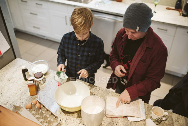 Отец и сын выпечки, глядя на рецепт на кухне — стоковое фото