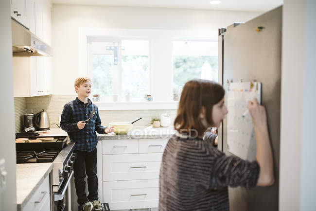 Brother and sister cooking and writing on calendar in kitchen — Stock Photo