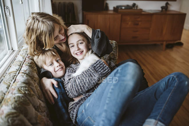 Retrato afectuoso madre e hijos con conejillo de indias en el sofá de la sala de estar - foto de stock