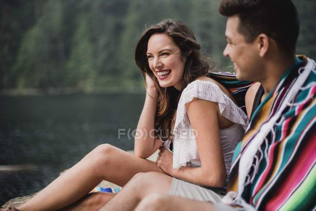 Feliz, jovem casal despreocupado envolto em um cobertor ao lado do lago — Fotografia de Stock