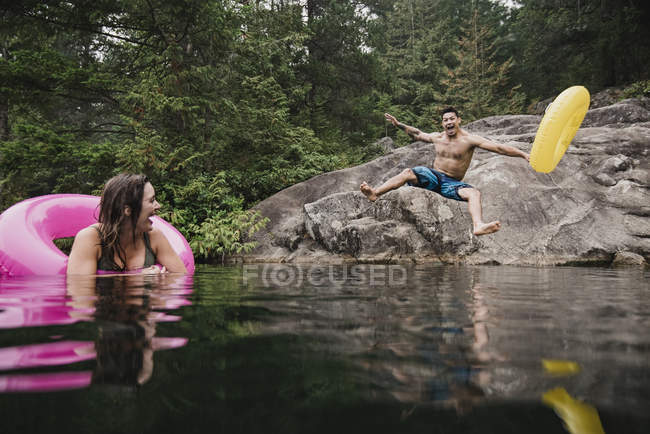 Giovane giocoso con anello gonfiabile che salta nel lago remoto, Squamish, British Columbia, Canada — Foto stock