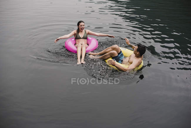 Young couple floating on lake in inflatable rings — Stock Photo