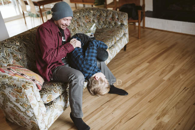 Père ludique tenant son fils à l'envers sur le canapé du salon — Photo de stock