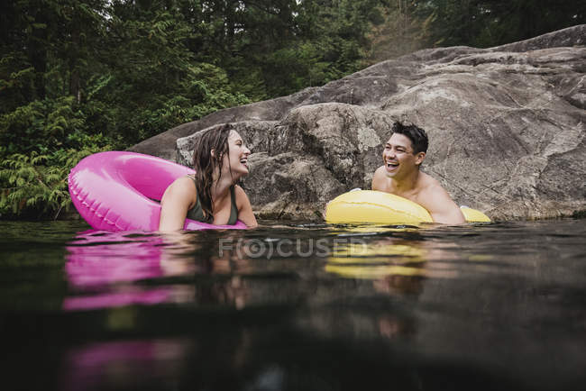 Felice giovane coppia galleggiante in anelli gonfiabili sul lago — Foto stock